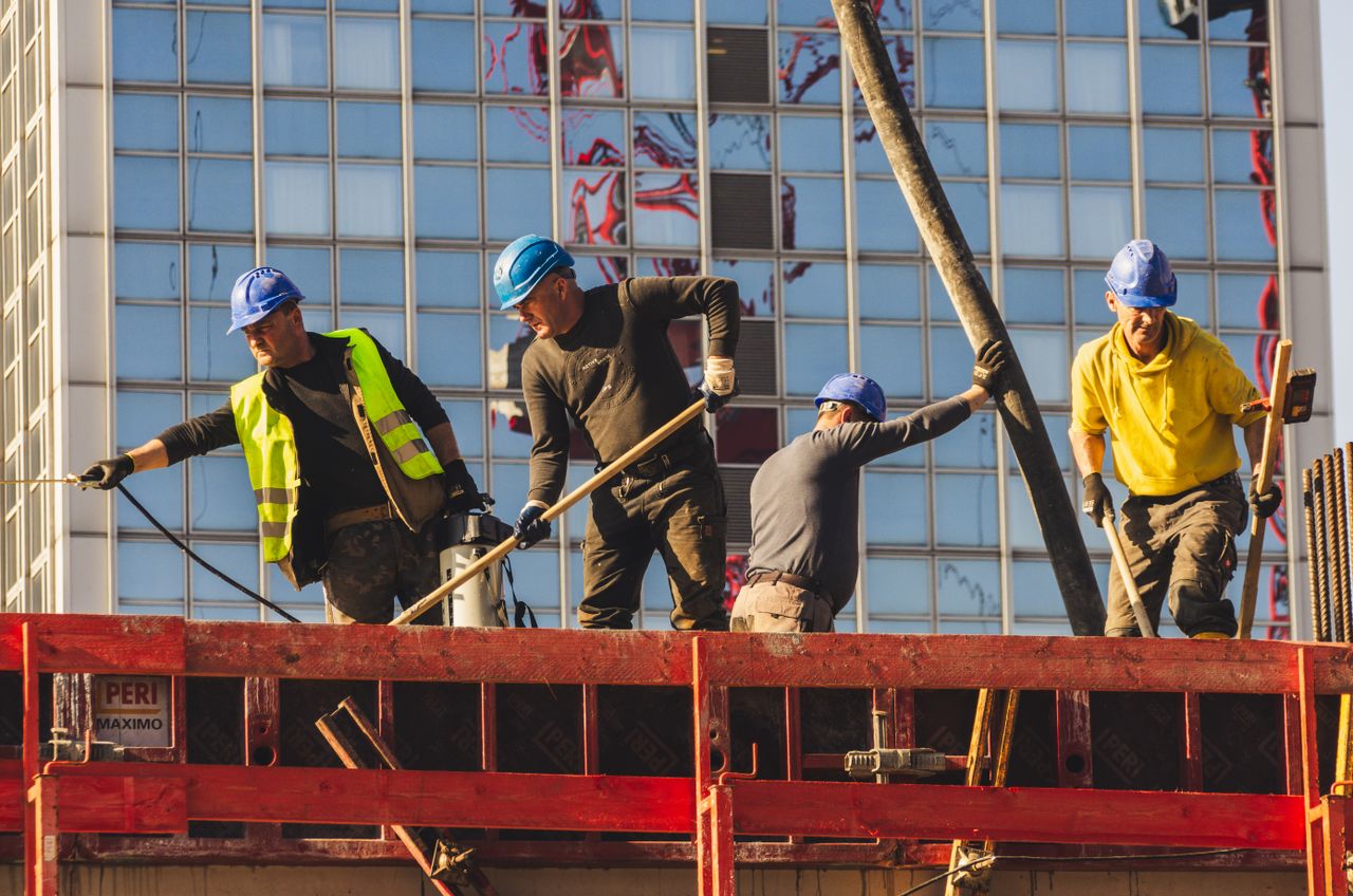 A group of construction workers in safety gear actively working on a high-rise building site.
