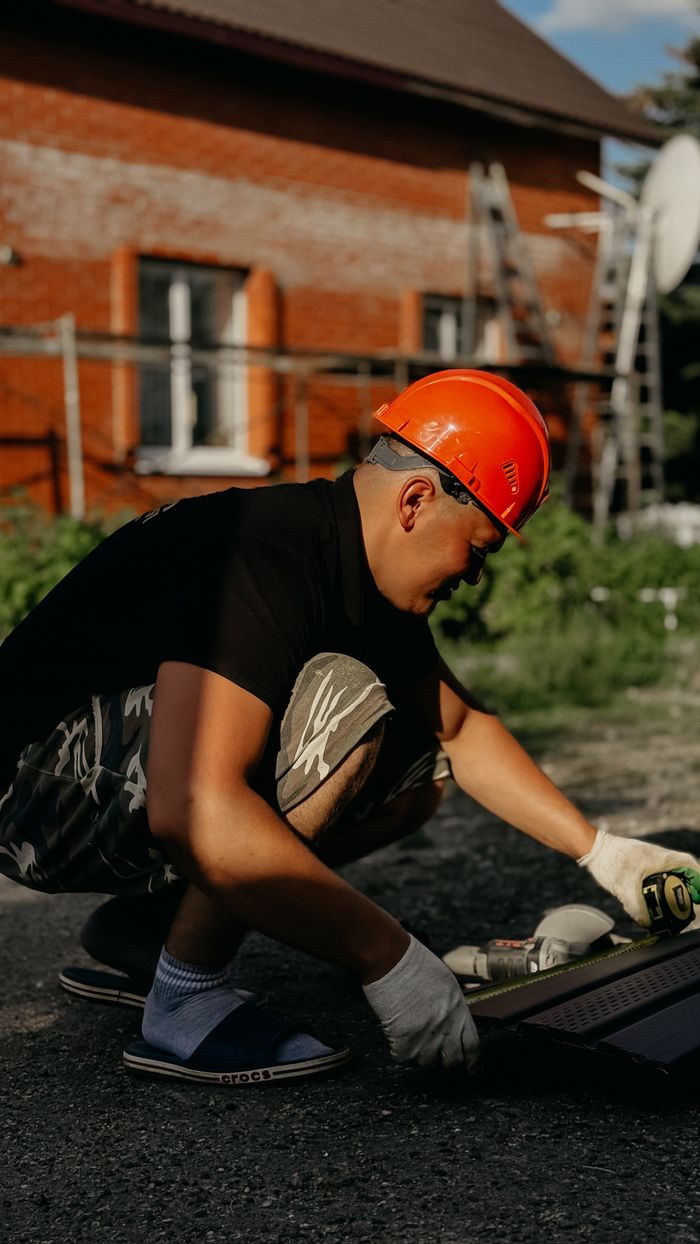 A construction worker wearing a hard hat working with tools outside a building.